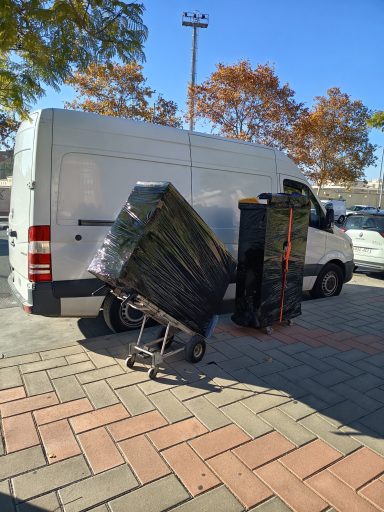 Furgoneta blanca aparcada con cajas apiladas y un carrito en una zona pavimentada.